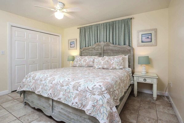 A bedroom with a bed, two bedside tables with lamps, a ceiling fan, and a door.