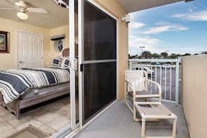 A bedroom with a bed, a sliding glass door, a ceiling fan, and a view of a parking lot.