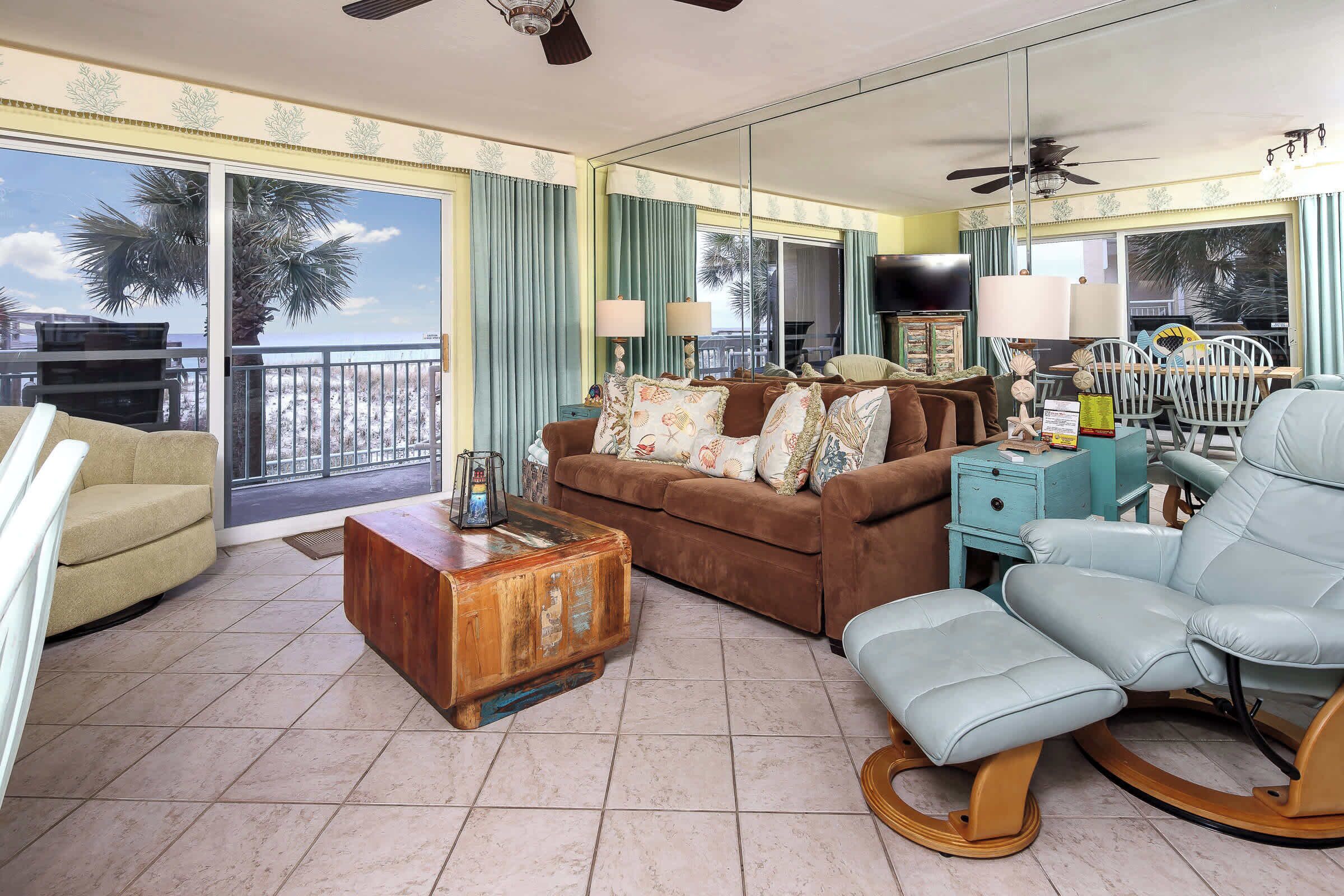 A living room with a brown sofa, a rocking chair, a wooden coffee table, and a view of the ocean through large windows.