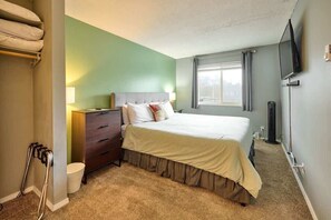 Une chambre à coucher avec un lit, une commode, une table de chevet, un téléviseur et une fenêtre.