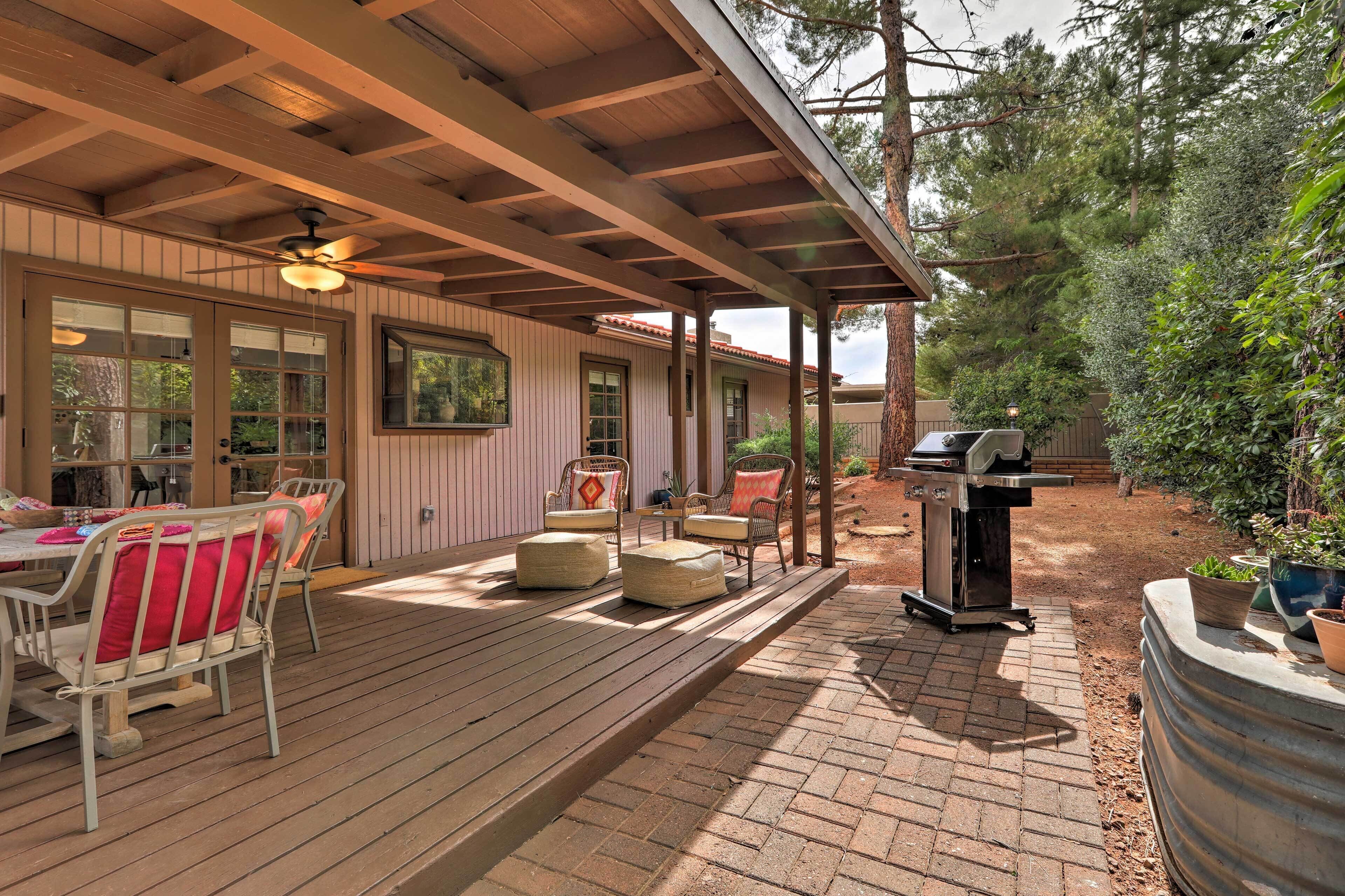 A covered outdoor patio with wooden flooring, a table with chairs, and a barbecue grill.