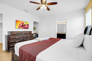 Une chambre à coucher comprenant un lit, une commode, un ventilateur de plafond, un téléviseur et un miroir avec éclairage intégré.