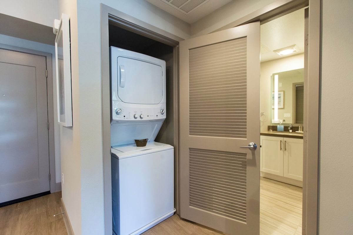 A laundry room with a washer and dryer, a door leading to a bathroom, and a hallway with a mirror.