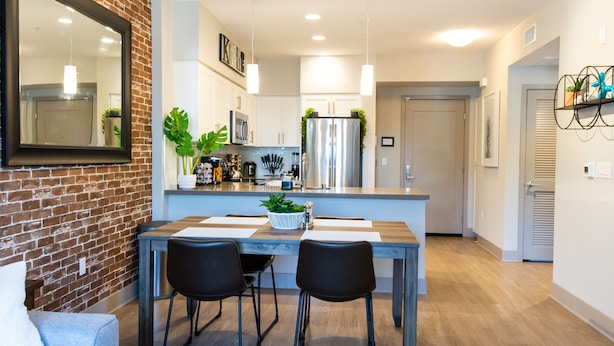 A modern kitchen with a brick wall, stainless steel appliances, and a dining area with two chairs and a table.