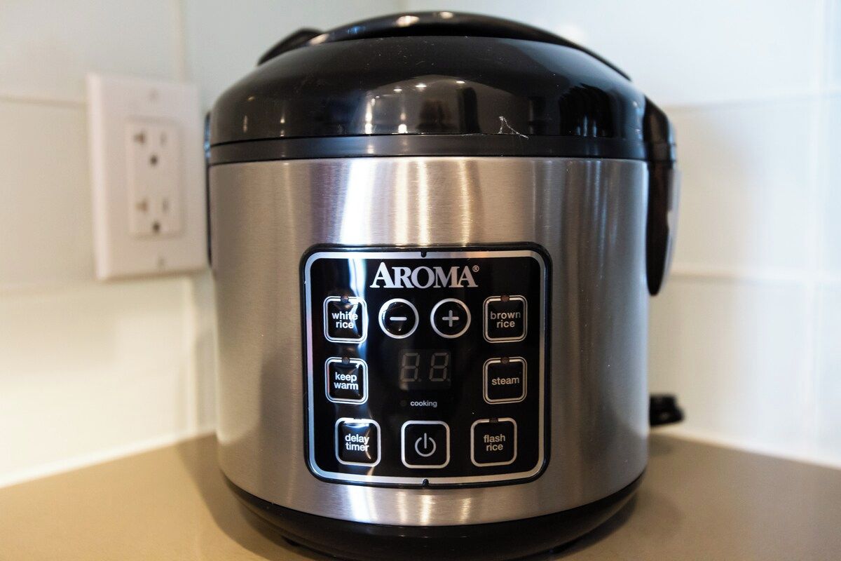A stainless steel AROMA rice cooker with a digital control panel.