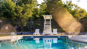 Una piscina con escalera, sillas de descanso y un área cercada.