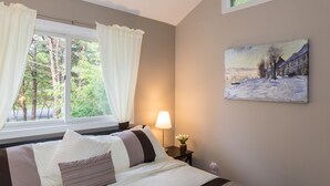 Une chambre à coucher avec un lit, une table de chevet, une lampe, un tableau et une fenêtre avec des rideaux.