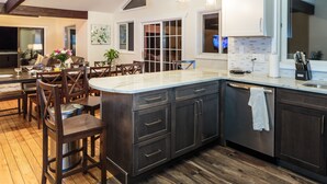 Une cuisine moderne avec des meubles de couleur sombre, un grand îlot central et un coin repas comprenant des chaises et une table en bois.