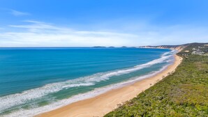 Un paysage côtier avec une plage de sable, une mer bleue et limpide, et des collines à l’horizon.