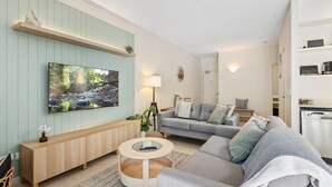 Un salon moderne doté d’un grand téléviseur à écran plat, d’un canapé gris, d’une console en bois et d’une table basse ronde.