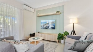 Un salon moderne avec un téléviseur fixé au mur, un canapé, une table basse et une lampe.