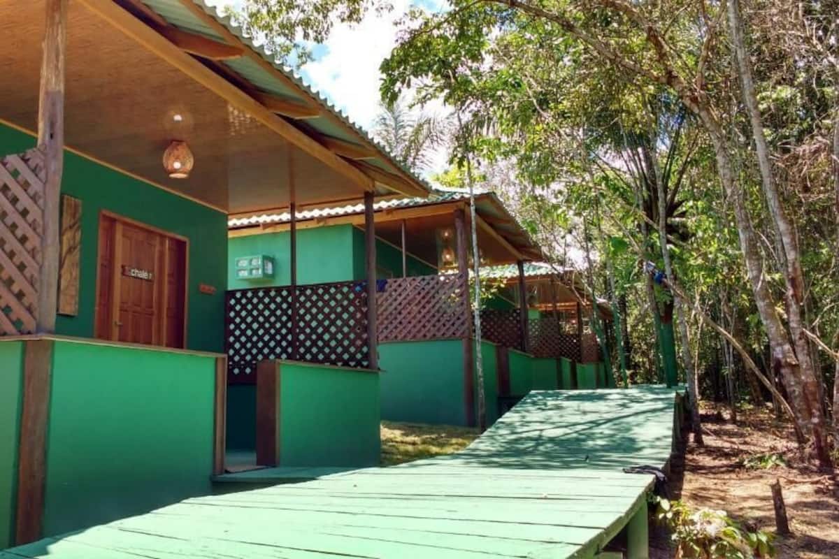 A row of green cabins with wooden beams and lattice railings, connected by a wooden deck.
