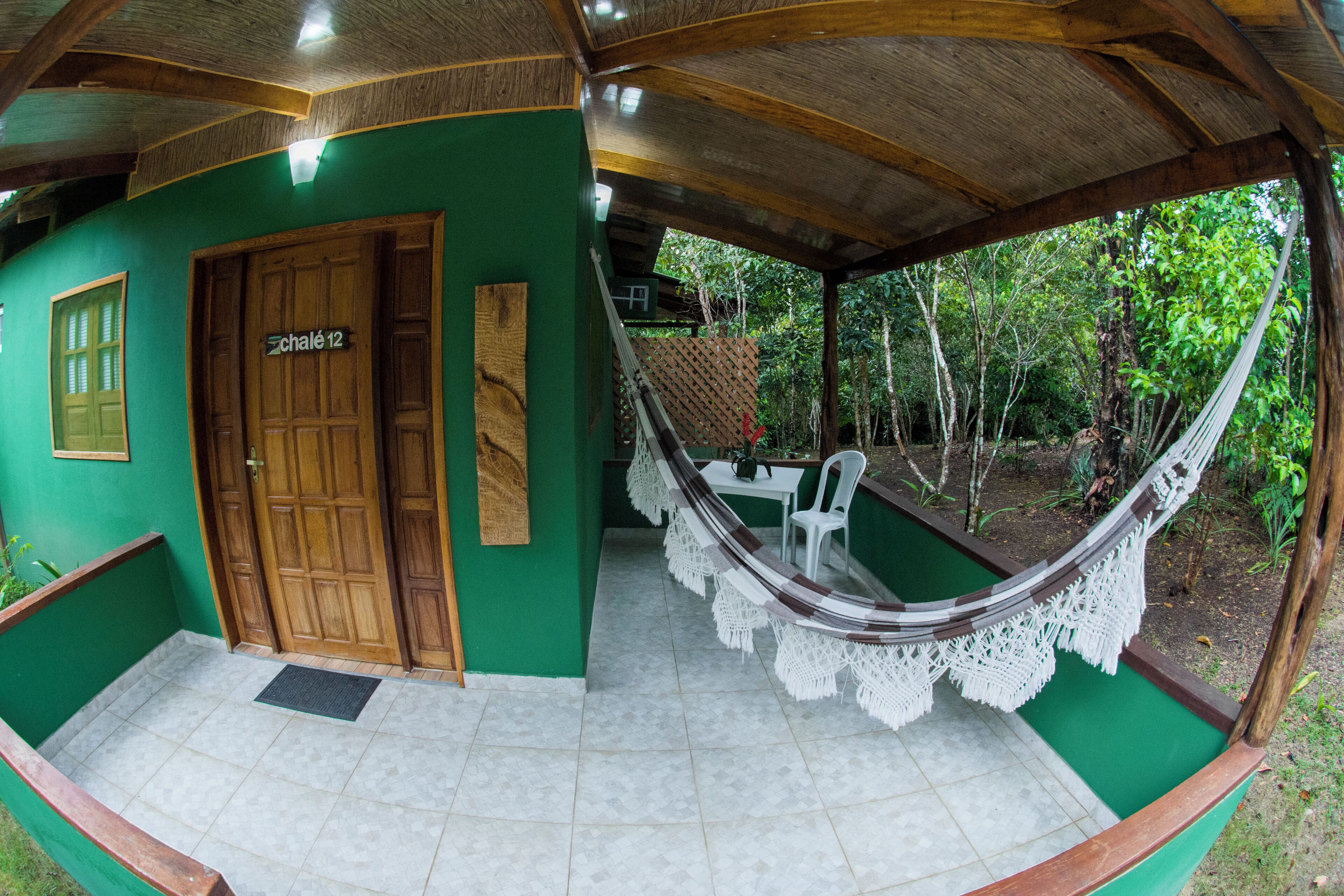 Uma rede sob um teto de madeira, uma porta com a inscrição "Chalet 12" e uma parede verde com uma janela.