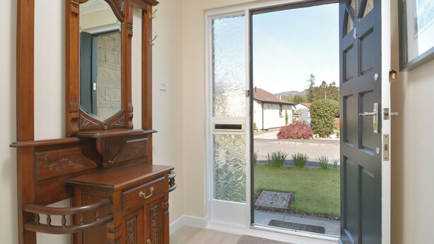 A wooden dresser with a mirror, a sliding glass door leading to a driveway, and a black door with a handle. - This lovely detached cottage is conveniently set all on one level. (Comrie, near Crieff)