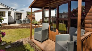 A covered patio area with wicker furniture, a wooden pergola, and a view of a white house with a patio and outdoor furniture. - This lovely detached cottage is conveniently set all on one level. (Comrie, near Crieff)