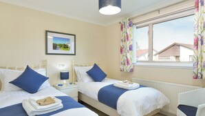 A twin room with two beds, a nightstand with a lamp, a framed picture, and a window with curtains. - This lovely detached cottage is conveniently set all on one level. (Comrie, near Crieff)