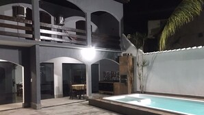 Uma área externa com vários níveis, piscina, mesa de jantar com cadeiras e escada para um andar superior.
