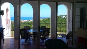 Un balcón con vistas al mar y follaje. Hay cuatro sillas y una mesa.