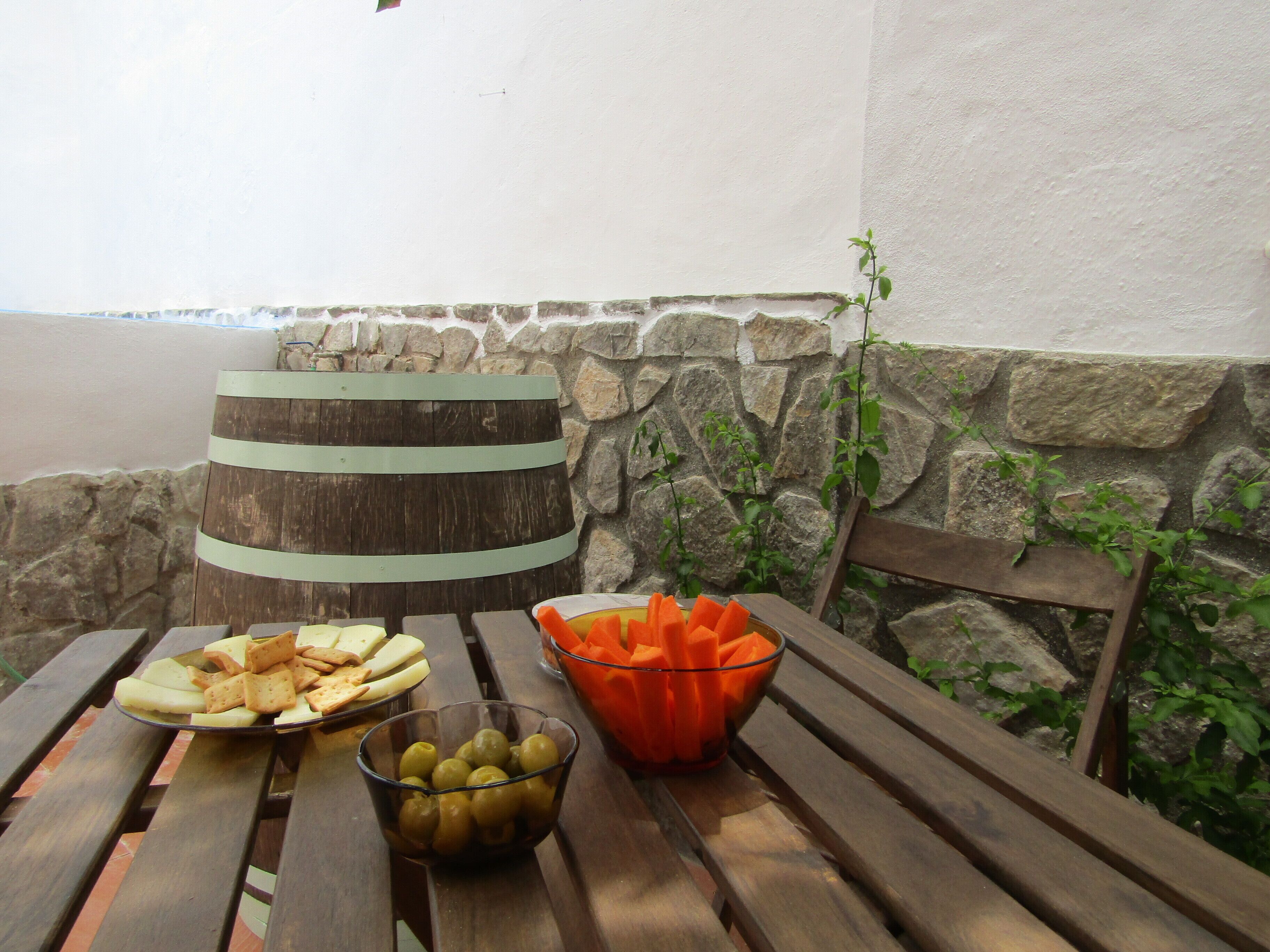 A wooden table with snacks, a glass bowl of olives, and a barrel.