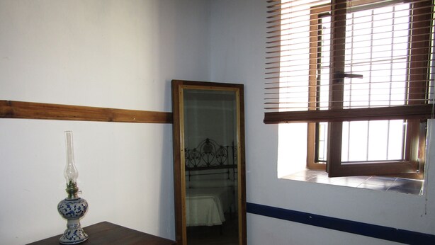 Une pièce avec une commode en bois, un miroir et une fenêtre avec des stores.
