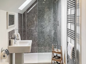 Un baño moderno con un lavamanos blanco, cabina de ducha con vidrio y repisa de madera con artículos de aseo.