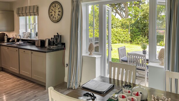 A kitchen with a clock, a dining table with chairs, and a view of the garden through large windows. - The Bay - The Bolthole (Filey, near Scarborough)