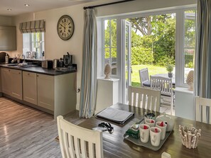A kitchen with a clock, a dining table with chairs, and a view of the garden through large windows. - The Bay - The Bolthole (Filey, near Scarborough)