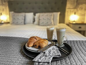 En pænt anrettet morgenmadsbakke med croissanter og to kaffekopper på en seng med et quiltet dynebetræk.