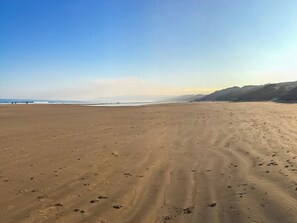 A wide sandy beach with footprints, a clear sky, and distant mountains.