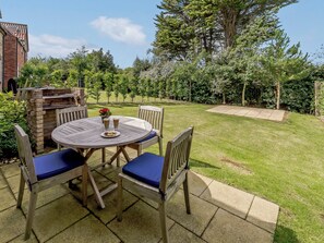 A patio with a round table and chairs, a brick barbecue, and a grassy yard with trees.