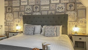 A neatly made bed with patterned pillows, a tray with croissants and coffee, and a wall decorated with framed pictures. - The Bay - The Bolthole (Filey, near Scarborough)