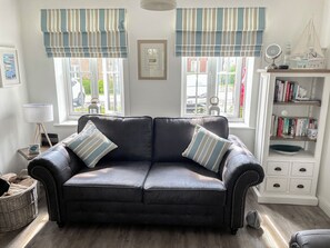A dark leather sofa with striped cushions, a white bookshelf with books, and a window with striped curtains.