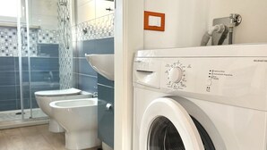 A modern bathroom with a washing machine, toilet, and glass shower enclosure. - M221 - Marcelli, new two-room apartment 100mt from the sea (Marcelli)