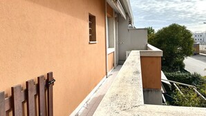A balcony with a wooden fence, a window, and a view of the street and greenery. - M221 - Marcelli, new two-room apartment 100mt from the sea (Marcelli)