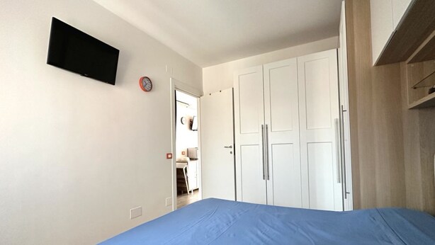 A bedroom with a bed, a flat-screen TV, white wardrobes, and a door leading to a bathroom. - M221 - Marcelli, new two-room apartment 100mt from the sea (Marcelli)
