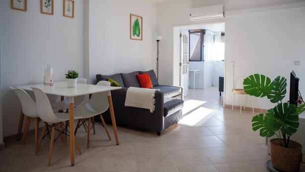 A modern living room with a grey sofa, white chairs, a dining table, and a large potted plant. - Just4uApartment 2 - Near Lisbon & Beach - With AC (Almada)