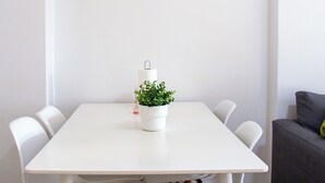 A dining area with a white table, four white chairs, and a potted plant. There are three framed botanical illustrations on the wall. - Just4uApartment 2 - Near Lisbon & Beach - With AC (Almada)