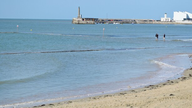 A beach with a pier, a lighthouse, and a building with a white facade.