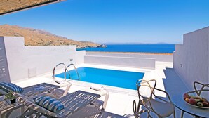 Zona junto a la piscina con vista al mar, sillones de descanso y una mesa con fruta.
