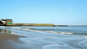 Een kustgezicht met een zandstrand, een gebouw met een groen dak en boten afgemeerd aan de oever.