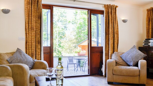 Een woonkamer met twee banken, een salontafel met glazen en een fles, en een glazen schuifdeur die leidt naar een buitenruimte met een tafel en stoelen.
