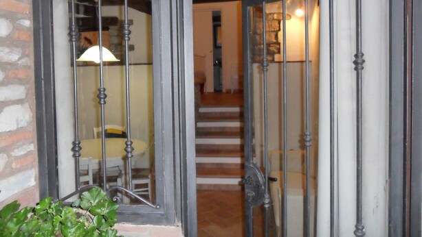 Una porta in legno con inferriate e un pannello di vetro, che dà accesso a una scala con un lampadario sopra.