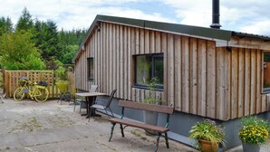 A wooden cabin with a bench and a table outside, surrounded by potted plants and a bicycle. - 2 bedroom accommodation in near Trecastle, Brecon (near Trecastle, Brecon)