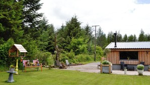 A rustic wooden cabin with a large window, surrounded by a well-maintained lawn and a variety of outdoor seating arrangements. - 2 bedroom accommodation in near Trecastle, Brecon (near Trecastle, Brecon)
