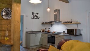 A modern kitchen with a built-in oven, microwave, and kettle. There is a wooden ceiling and a wall-mounted clock. - 2 bedroom accommodation in near Trecastle, Brecon (near Trecastle, Brecon)