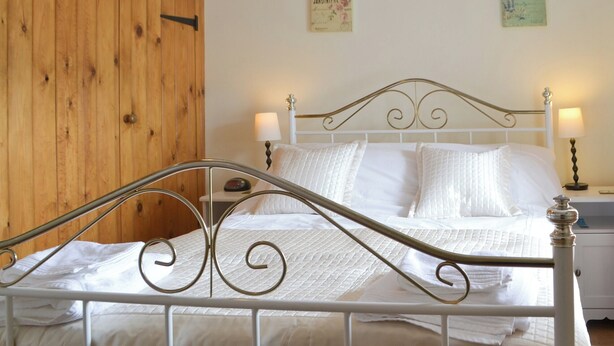 Una cama bien hecha con ropa blanca y estructura metálica, una puerta de madera y dos lámparas de pared a cada lado.