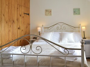 A neatly made bed with white linens and a metal frame, a wooden door, and two wall-mounted lamps on either side of the bed.