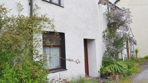 Una casa blanca con un pequeño jardín delantero, una ventana con cortina y una antena parabólica.