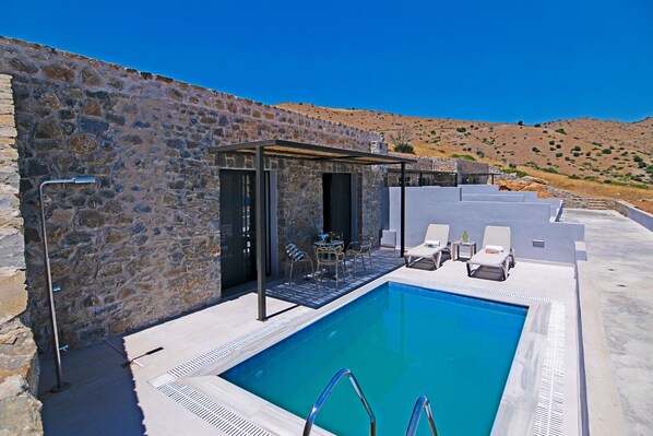 A pool area with a stone wall, lounge chairs, and a covered seating area. - Varkotopi villa 1,Pool,Near the Beach,South Crete (Rethymno)
