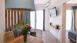 Ett modernt matområde med ett träbord, flätade stolar, en vas med blommor, en hängande lampa och en tv som är monterad på väggen.